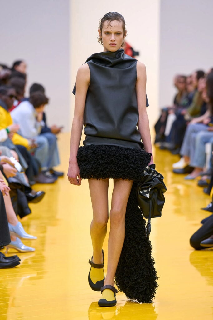 A model wears the black sculpted leather and shearling-trimmed dress on the Loewe Fall 2026 runway.