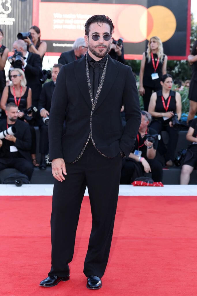 Miguel Ćngel Silvestre wearing a black Giorgio Armani suit with shimmering trim at the 2026 Venice Film Festival.