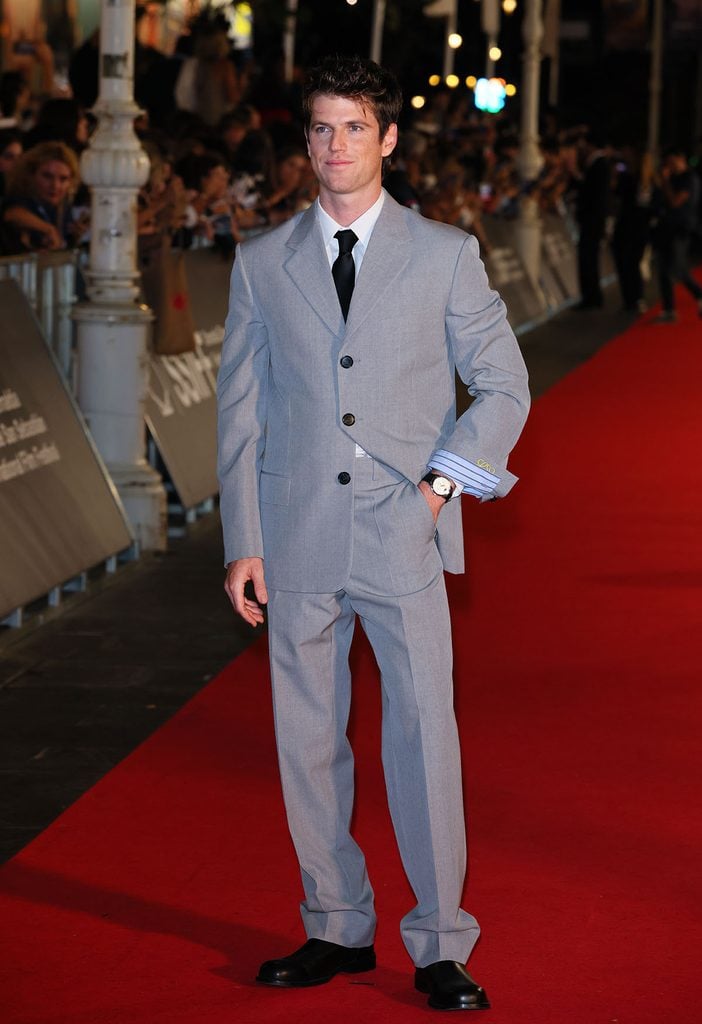 Miguel Bernardeau wearing a grey Loewe suit with a white shirt, black tie and turned-up monogrammed cuff at the La Bola Negra premiere in San Sebastián