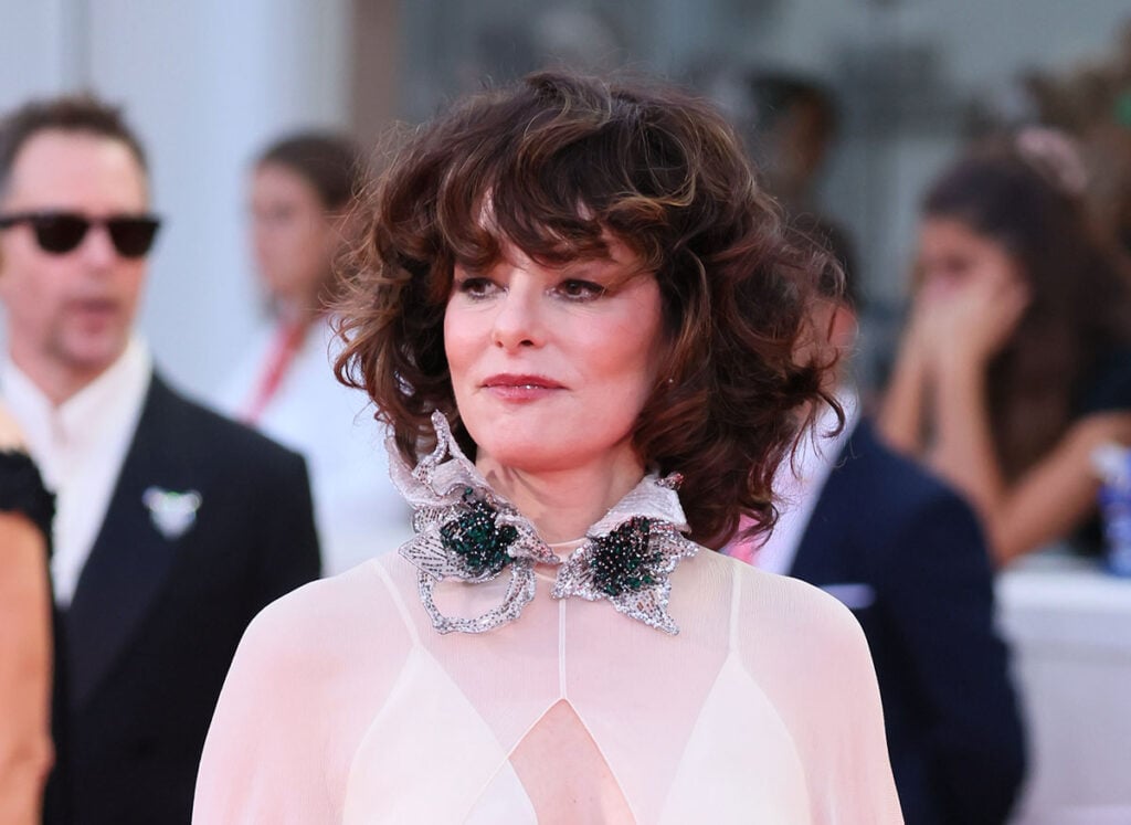 Parker Posey wearing a pale-pink Valentino Resort 2027 crystal-and-emerald embellished collar.