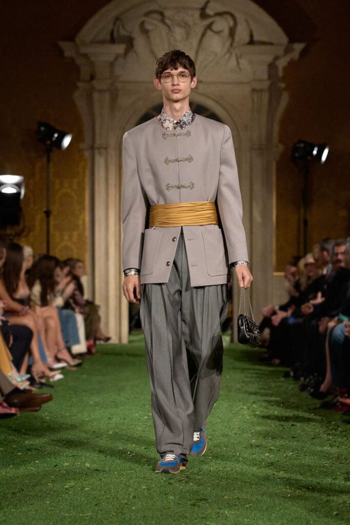 Valentino Fall 2026 runway look featuring the grey jacket with frog closures and gold waist sash worn by Kingston Rumi Southwick.