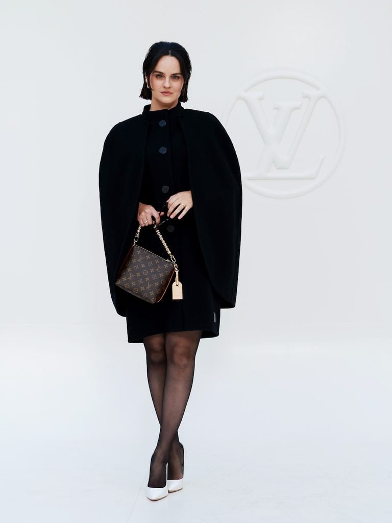 Noémie Merlant wearing a black Louis Vuitton cape-style mini coat at the Spring-Summer 2027 show in Paris.