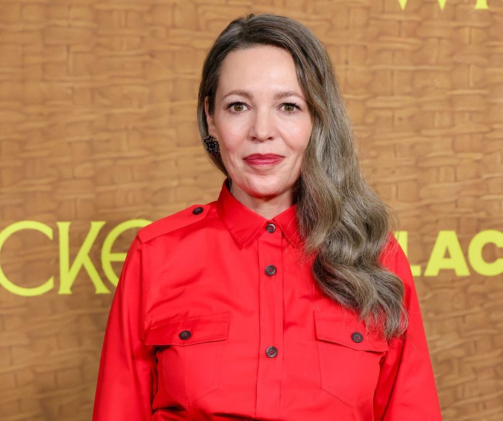 Olivia Colman long grey hair wearing a red Prada utilitarian shirt and burgundy taffeta skirt with an asymmetric train at the Wicker premiere in Los Angeles.