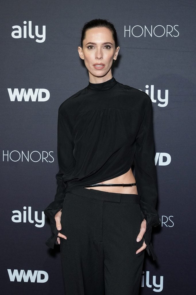 Rebecca Hall attends the WWD Honors in a black Tom Ford Fall 2026 ensemble featuring a high-neck top, asymmetric waist cut-out and wide-leg trousers, accessorised with a KATKIM earring and black clutch.
