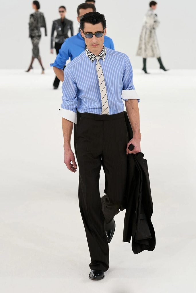 Tom Ford Fall 2026 runway model in a blue striped shirt with an animal-print collar, striped tie and black trousers, a look later worn by Aaron Taylor-Johnson.