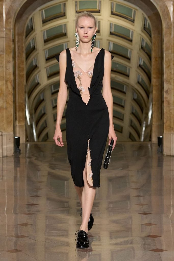 Altuzarra Spring 2027 runway model wearing the black dress with sheer floral-embroidered panels and mismatched earrings later worn by Michelle Monaghan.