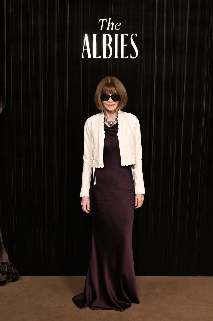 Anna Wintour wearing a plum satin gown with a cropped ivory jacket and statement necklace at the 2026 Albies in London