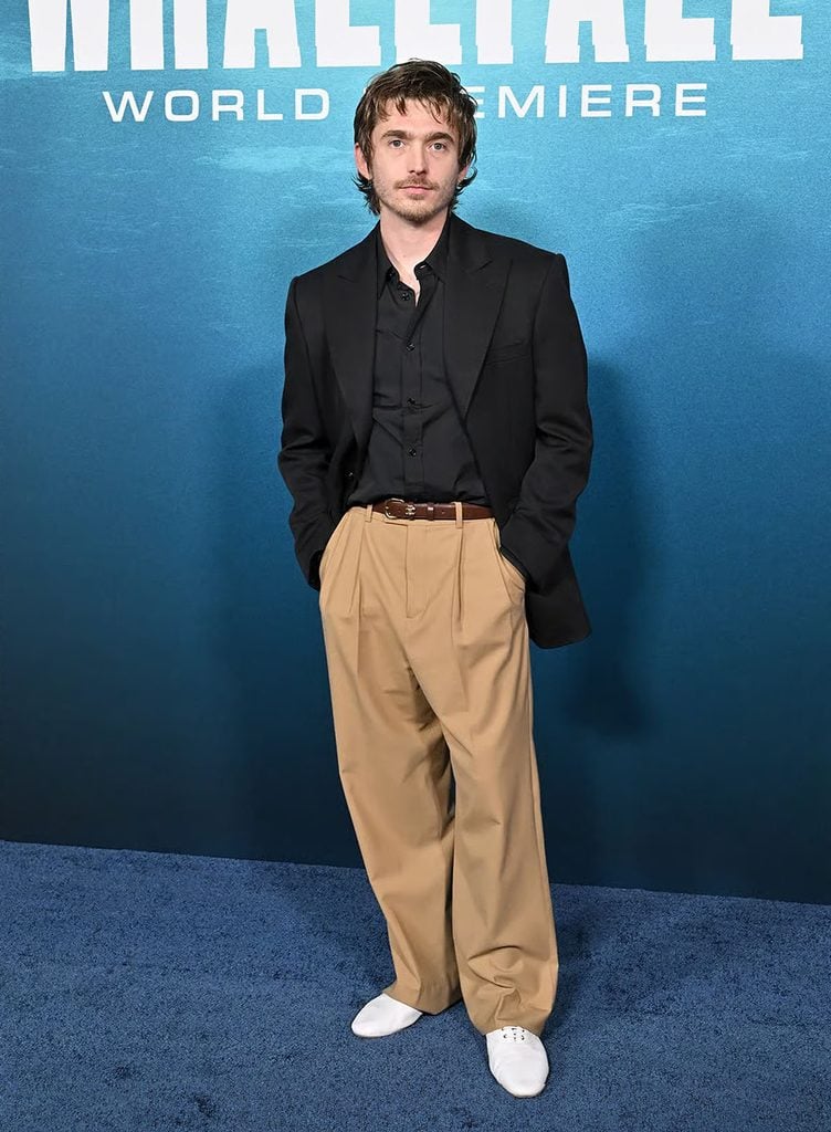 Austin Abrams wearing a black Celine blazer and shirt with camel pleated trousers and white shoes at the 'Whalefall' Los Angeles premiere.