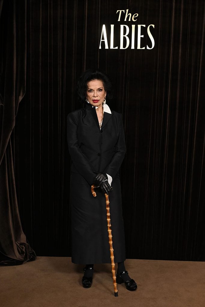 Bianca Jagger wearing a black tailored Gucci ensemble with leather gloves and a bamboo walking cane at the 2026 Albies.