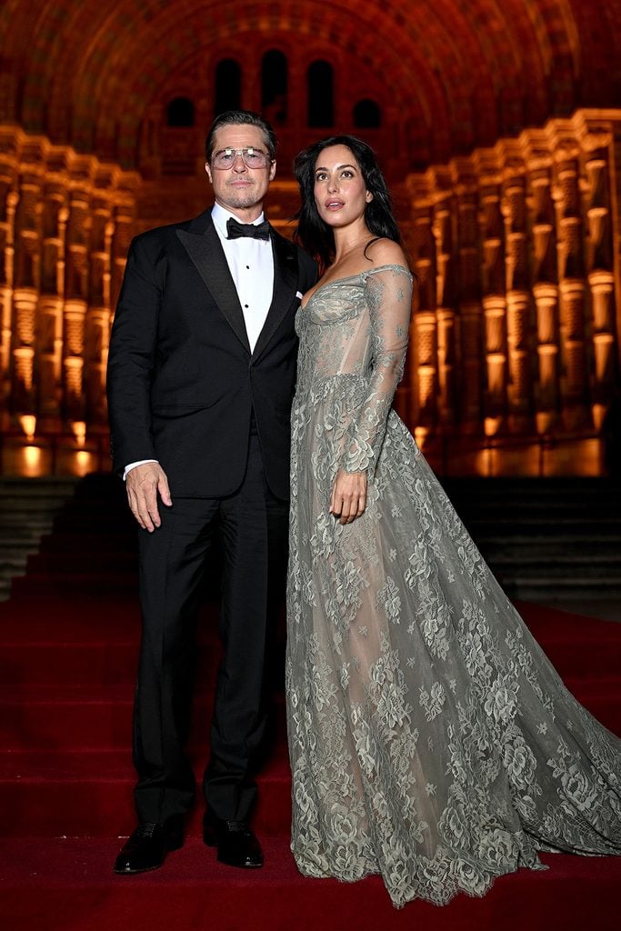 Brad Pitt wearing a black tuxedo and Jacques Marie Mage aviator sunglasses alongside Ines de Ramon in a sheer grey-green floral lace gown at the 2026 Albies in London.