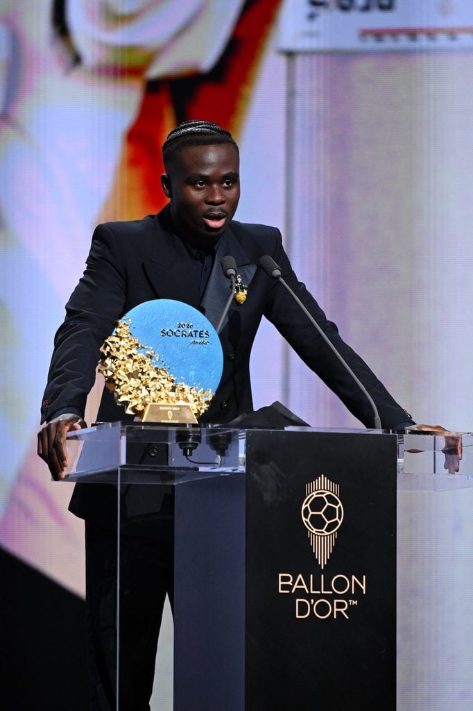 Bukayo Saka accepting the Sócrates Award in a Wales Bonner Spring 2027 suit with a Compass Brooch at the 2026 Ballon d'Or ceremony.