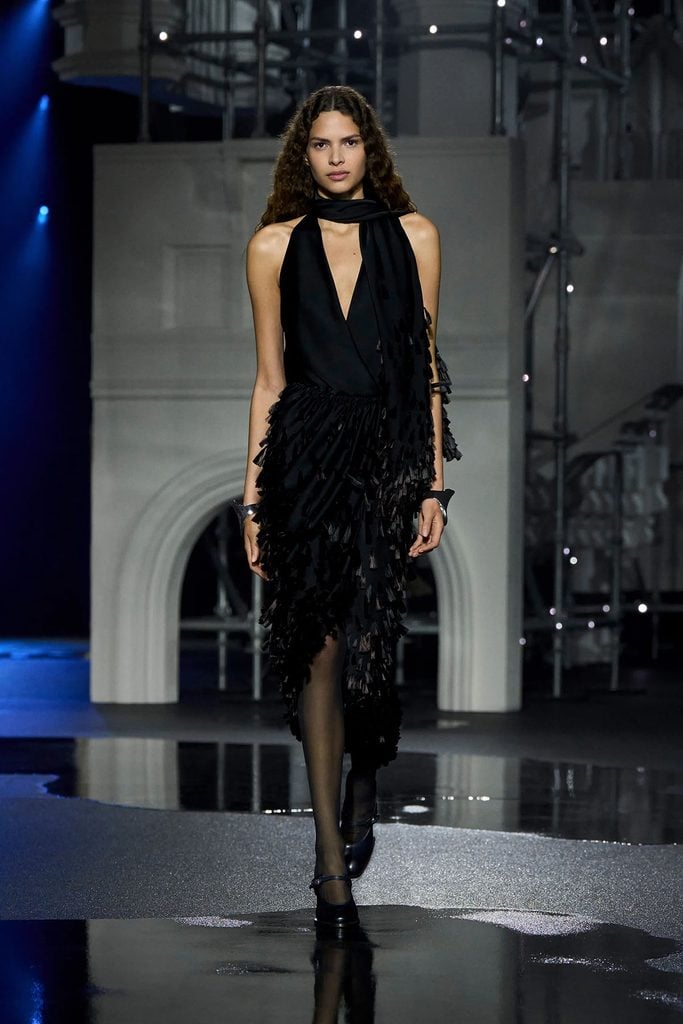 Burberry Fall 2026 runway model wearing the black satin version of Gemma Chan's scarf-detailed dress with textured tassels.