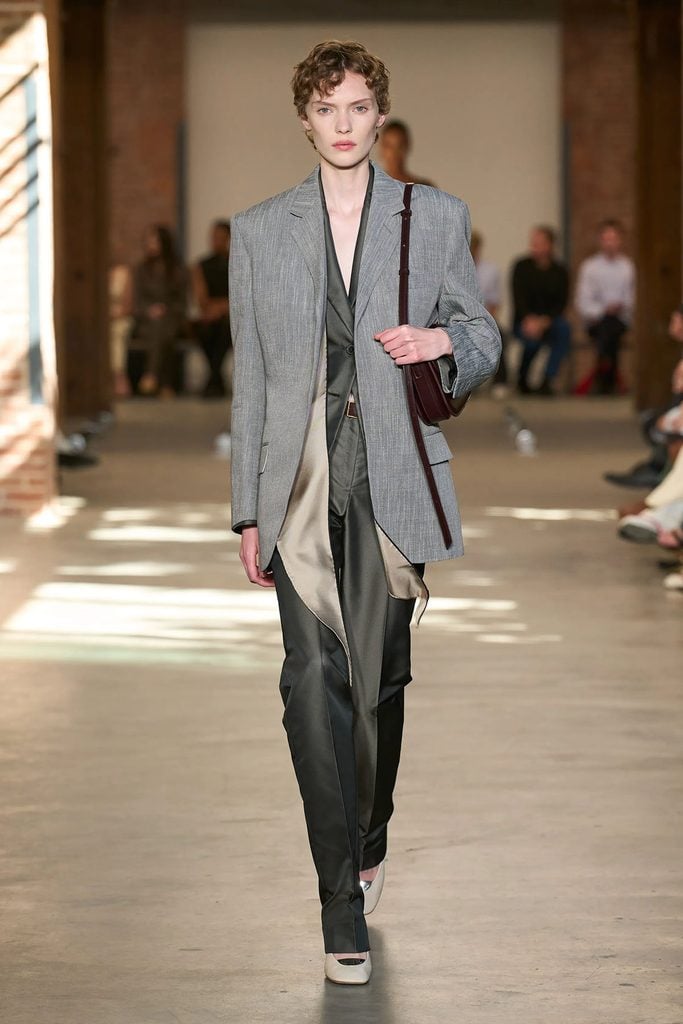 Calvin Klein Collection Spring 2027 runway look 17 featuring layered grey tailoring, a silk scarf and off-white pumps, as worn by Louisa Jacobson in New York.