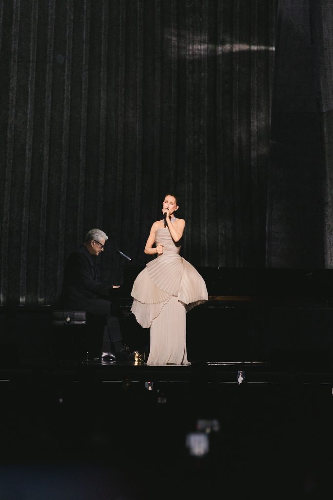 Céline Dion wearing a champagne Dior gown with a pleated bodice and sculptural waist during her Paris concert.