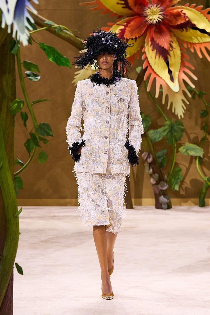 Chanel Fall 2026 Haute Couture runway model wears the ivory embroidered skirt suit with black feathered hat and gold pumps later worn by Dua Lipa at the WSJ. Magazine Innovator Awards.