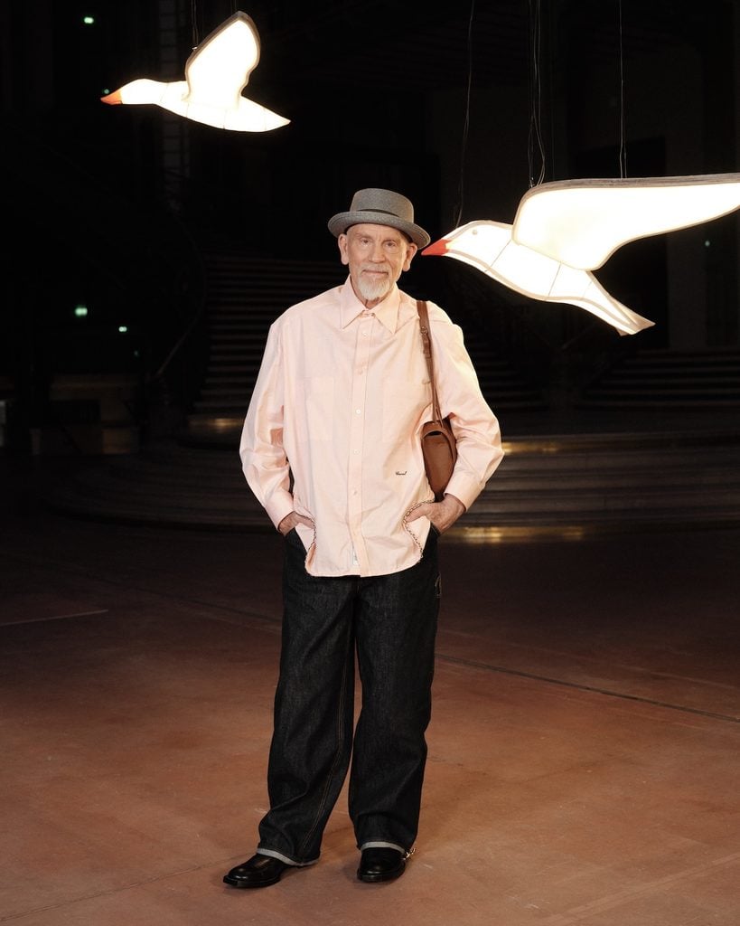 John Malkovich wearing a pale-pink Chanel shirt with dark jeans at the Chanel Spring 2027 show during Paris Fashion Week.