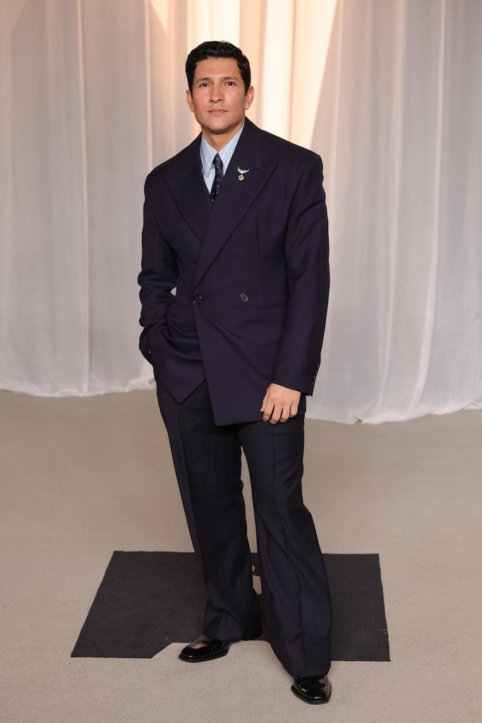 Danny Ramirez wearing tonal navy Saint Laurent tailoring with a Tiffany & Co. Bird on a Rock brooch at the 2026 Academy Museum Gala