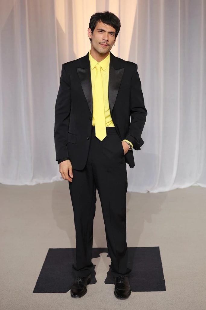 Diego Calva wearing a black Loewe tuxedo with a bright yellow shirt and matching tie at the 2026 Academy Museum Gala in Los Angeles.
