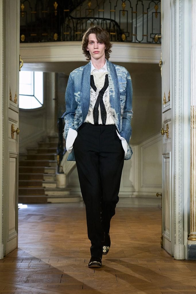 Dior Spring 2027 menswear runway look featuring a distressed blue denim jacket, embroidered ivory shirt, black sequinned tie and black trousers