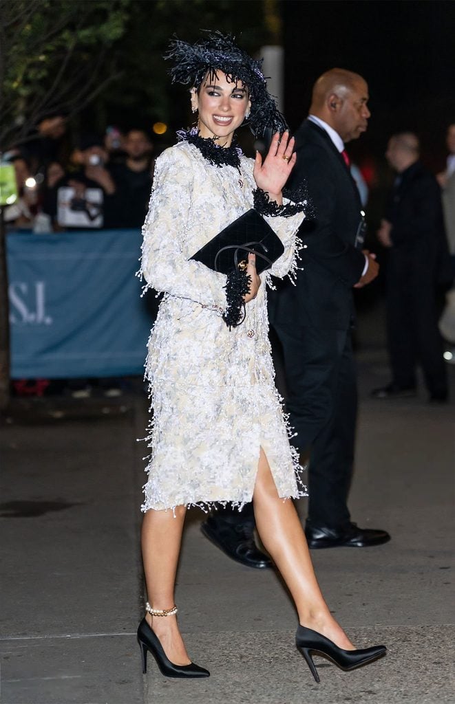 Dua Lipa smiles and waves outside the WSJ. Magazine Innovator Awards, carrying a black quilted Chanel clutch with her ivory couture skirt suit.