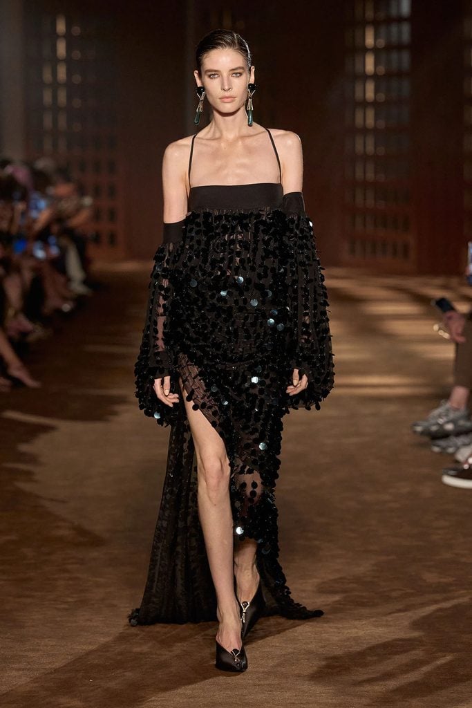 Ferragamo Spring 2027 runway look 61 featuring a sheer black chiffon dress with three-dimensional paillettes, an asymmetric hemline and a trailing train.