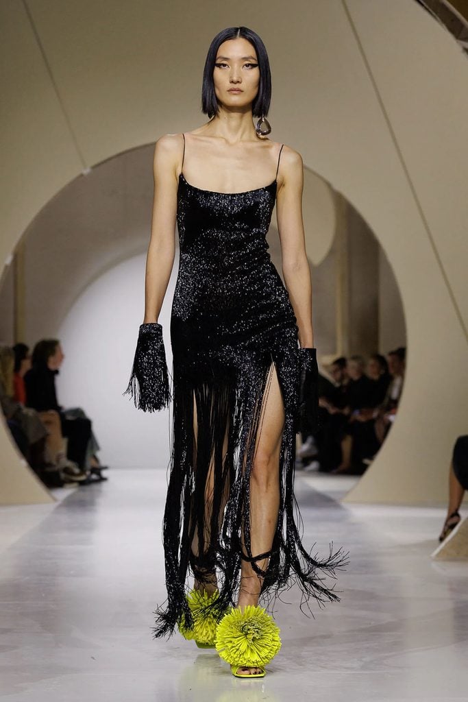 Givenchy by Sarah Burton Spring 2027 runway look featuring a black embroidered fringe dress styled with bright green floral sandals.