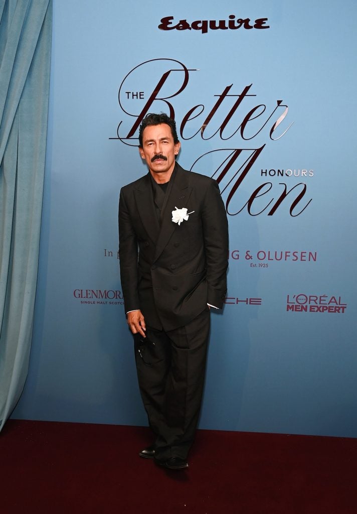 Haider Ackermann wearing black Tom Ford tailoring with a white floral brooch at Esquire UK's Better Men Honours at Claridge's in London.