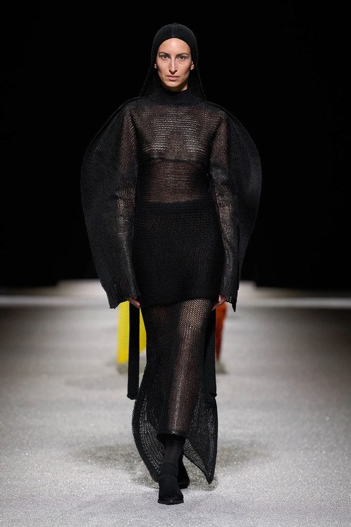 Issey Miyake Fall 2026 runway look featuring an oversized sculptural black knitted dress with exaggerated sleeves and a longer skirt.