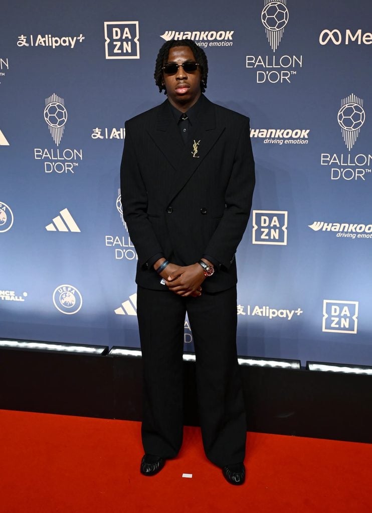 Johan Manzambi wearing a black Saint Laurent double-breasted suit with a gold brooch at the 2026 Ballon d'Or Awards.