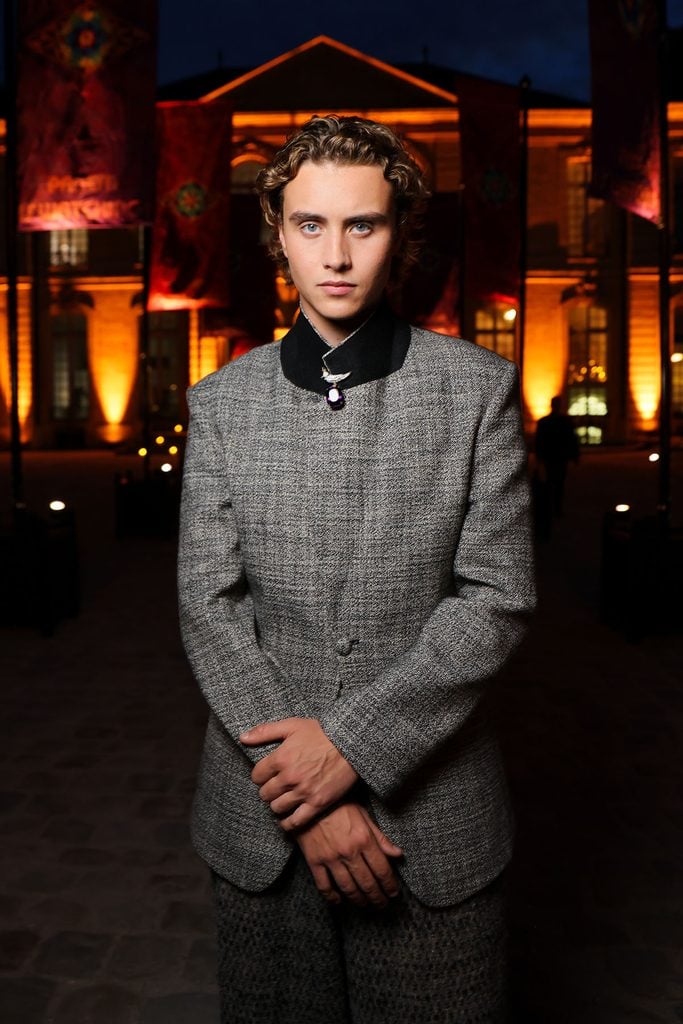 Joseph Zada wearing a grey ERL suit with a Tiffany & Co. Bird on a Rock brooch at the Hunger Games event in Paris.