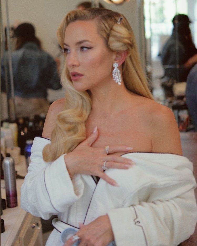 Kate Hudson backstage before the Academy Museum Gala, showing her side-swept blonde waves and hair clips during styling by Renato Campora.