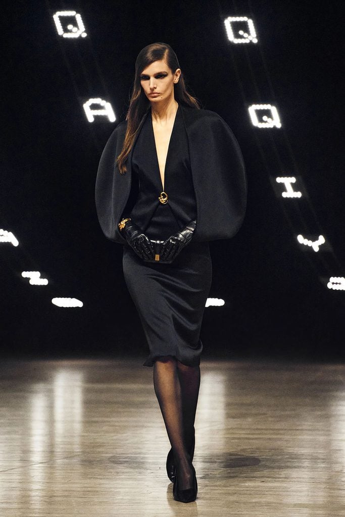 Khaite Fall 2026 runway model wears the black Dakota crepe-satin dress with oversized rounded sleeves, a gold neckline fastening and leather gloves.