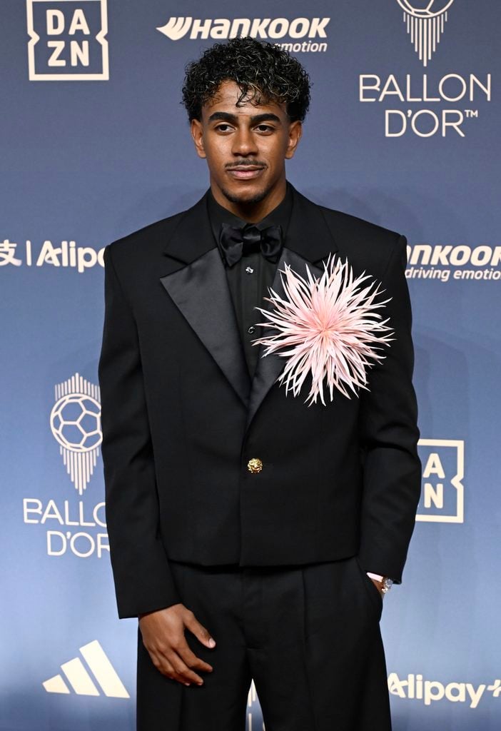 Lamine Yamal wearing a black Chanel cropped suit with an oversized pink feather camellia at the 2026 Ballon d'Or Awards.