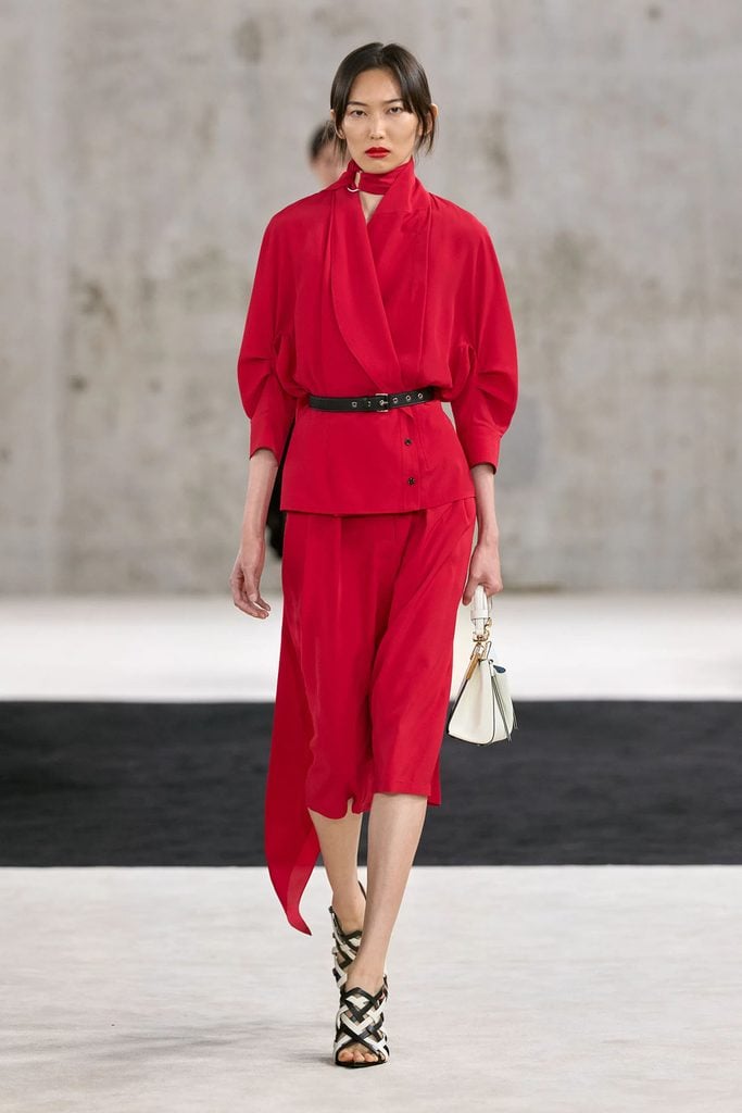 Lanvin Spring 2027 runway model wearing the red belted jacket and asymmetric skirt styled with strappy sandals and a white handbag