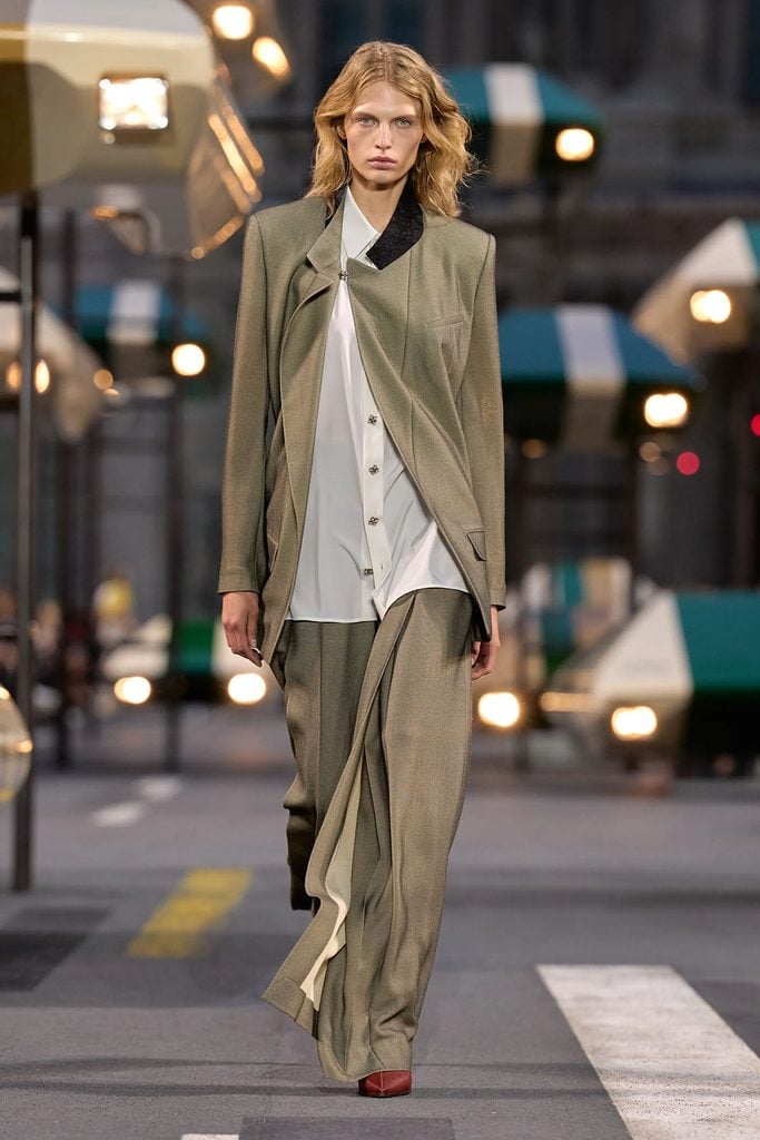Louis Vuitton Spring 2027 runway model wearing a grey asymmetric jacket, white silk shirt and draped trousers with red leather shoes.