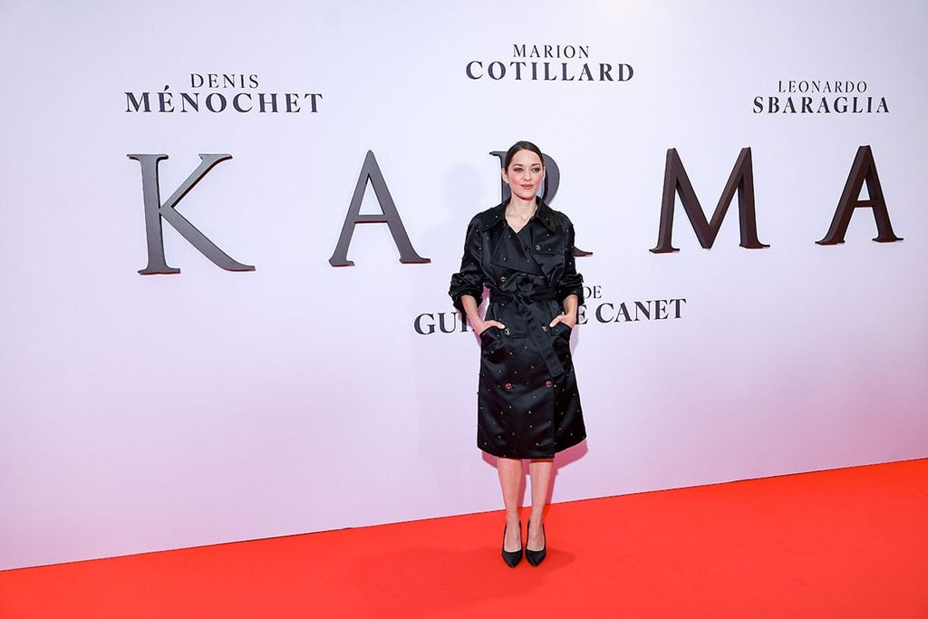 Marion Cotillard showing the green and silver embellishments, CC buttons and belted waist of her black Chanel trench coat at the 'Karma' Paris photocall.
