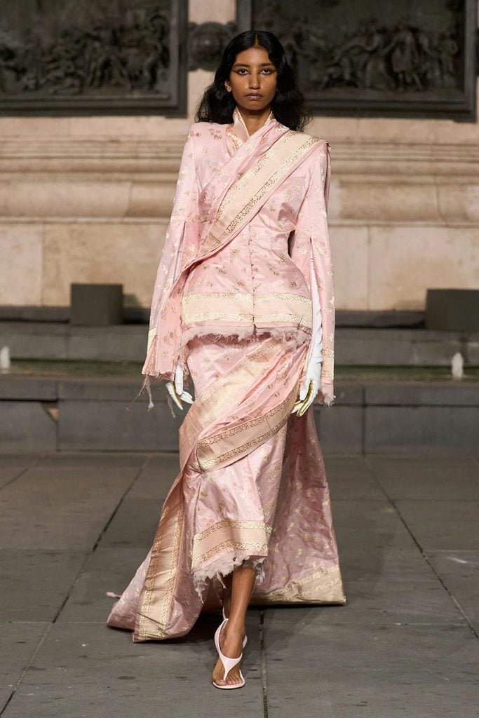 Matières Fécales Spring 2027 runway model wearing the pink floral satin ensemble with diagonal sari-inspired draping and a trailing skirt.