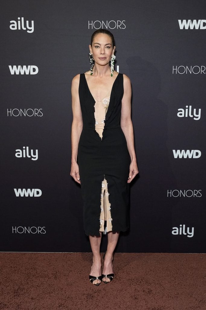 Michelle Monaghan wears a black Altuzarra Spring 2027 dress with floral-embroidered sheer panels and statement earrings at the 2026 WWD Honors.