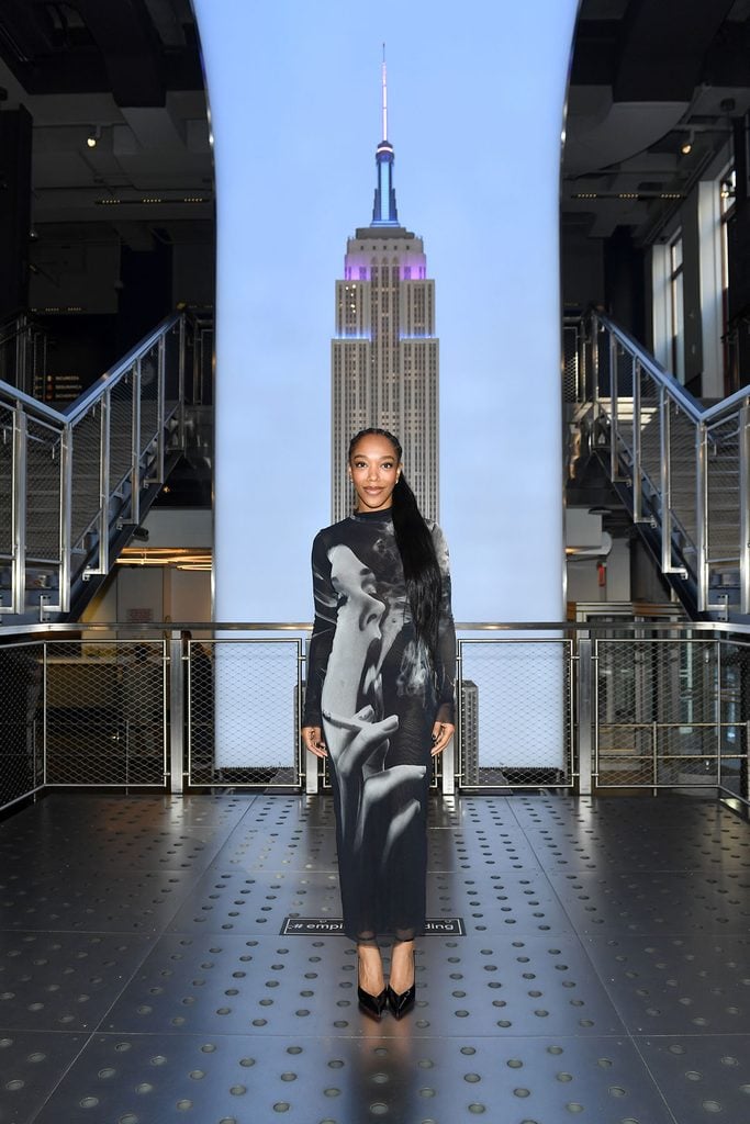 Naomi Ackie wears a Jean Paul Gaultier Smoking Graphic mesh bodycon dress during a Clayface promotional visit to the Empire State Building in New York in background