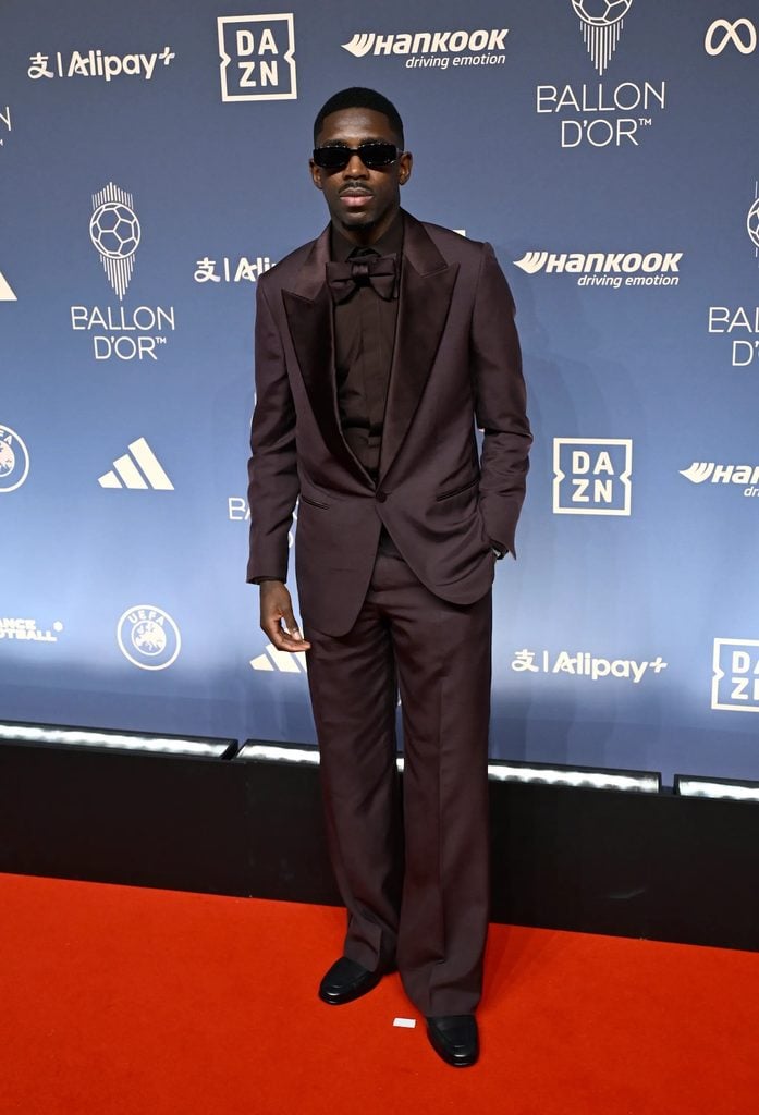 Ousmane Dembélé wearing a burgundy tuxedo with a matching bow tie and sunglasses at the 2026 Ballon d'Or Awards.
