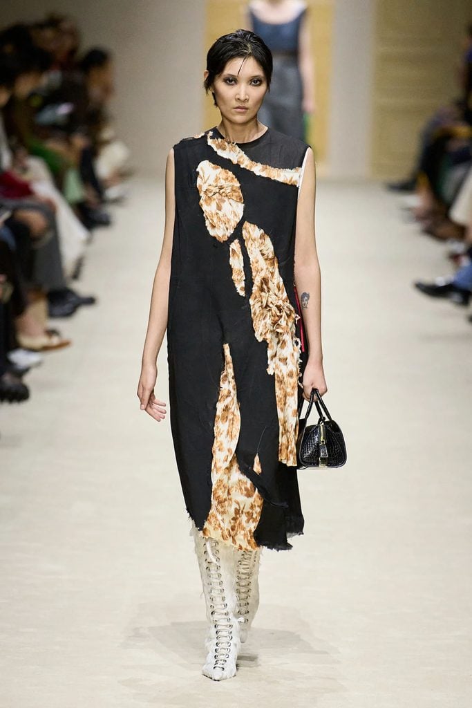 Model wearing a black and floral distressed dress with white lace-up boots and a black handbag on the Prada Fall 2026 runway.