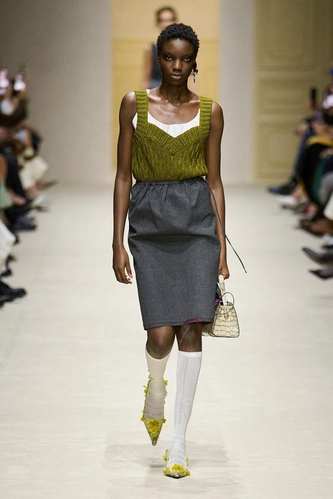 Model wearing the olive-green knit top and grey distressed-hem skirt from the Prada Fall 2026 runway collection.