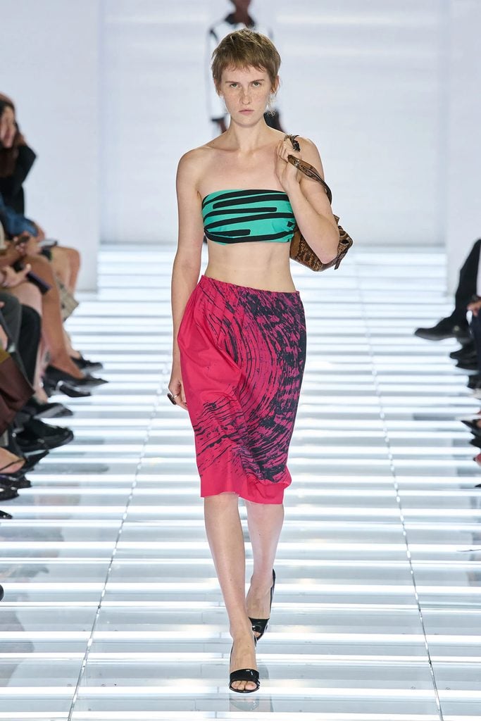 Model wearing a turquoise-and-black striped bandeau top with a pink printed skirt and black mules on the Prada Spring 2027 runway.