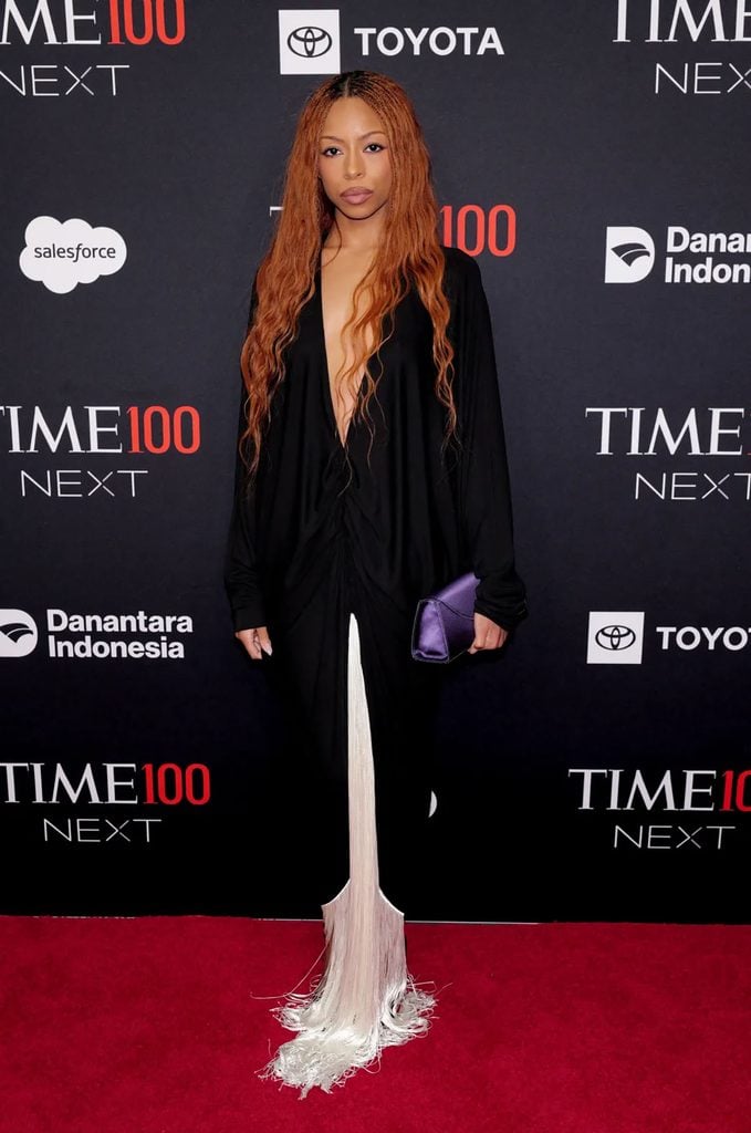 Ravyn Lenae wears an Ilkyaz Ozel black plunging maxi dress with floor-length white fringe and carries a purple Reformation clutch at the TIME100 Next Gala.