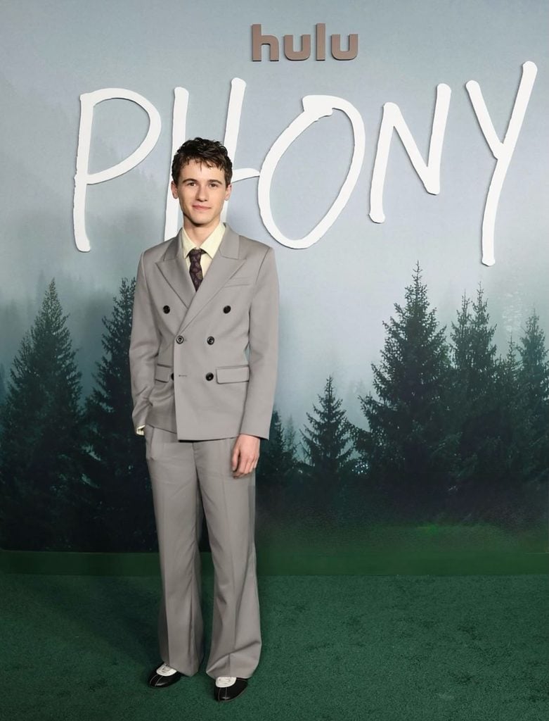 Sam Nivola wearing a grey Pearled Ivory double-breasted suit, patterned tie and black-and-white adidas Y-3 shoes at the 'Phony' Los Angeles premiere.
