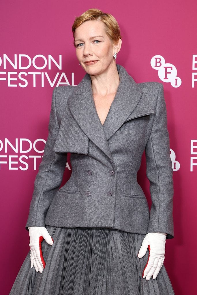 Sandra Hüller wearing a grey Matières Fécales Fall 2026 tailored jacket with sculpted shoulders and white gloves with red detailing at the ‘Rose’ BFI London Film Festival screening.