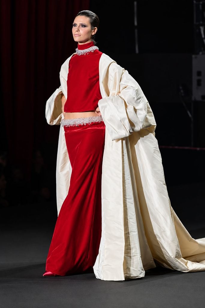 Model wearing a red velvet two-piece ensemble with a voluminous ivory coat from Stéphane Rolland Haute Couture Fall 2026 on the runway.