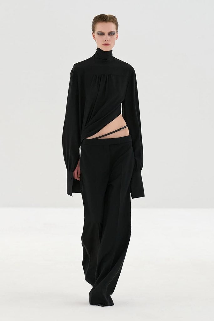 Tom Ford Fall 2026 runway model wearing the black high-neck top and cut-out trousers with a leather belt later worn by Rebecca Hall.