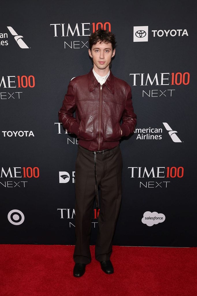 Troye Sivan wears a burgundy Prada leather jacket with dark brown trousers and a long hanging belt at the 2026 TIME100 Next Gala.