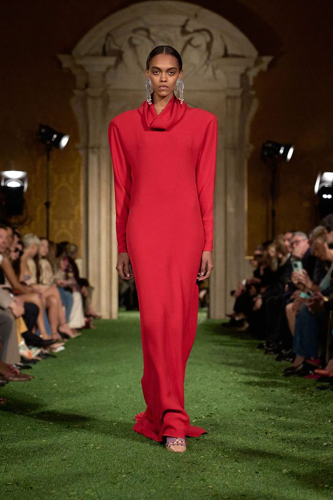 Model wearing a red long-sleeved gown with a draped neckline on the Valentino Fall 2026 runway.